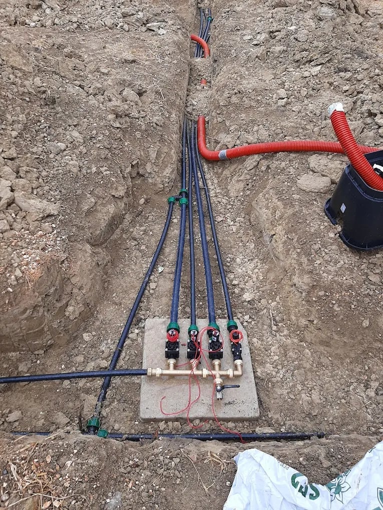 Electrical conduit and wiring with circuit breakers mounted on wooden board in dirt, connected to red conduit above